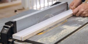 worker is using table saw to cut piece of wood dust is visible on table surface on carpentry work